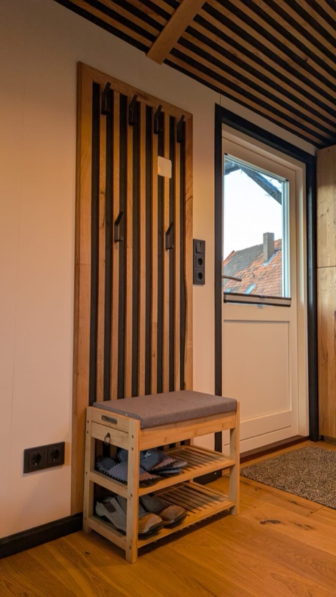 Eingangsbereich mit Garderobe aus Holzlatten, Sitzbank und Tür mit Fenster.