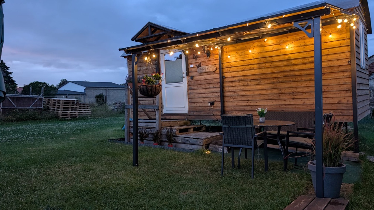 Der Bauwagen von Brinkman baut's am Abend, warm beleuchtet von einer Lichterkette, mit gedeckter Sitzecke im Grünen.